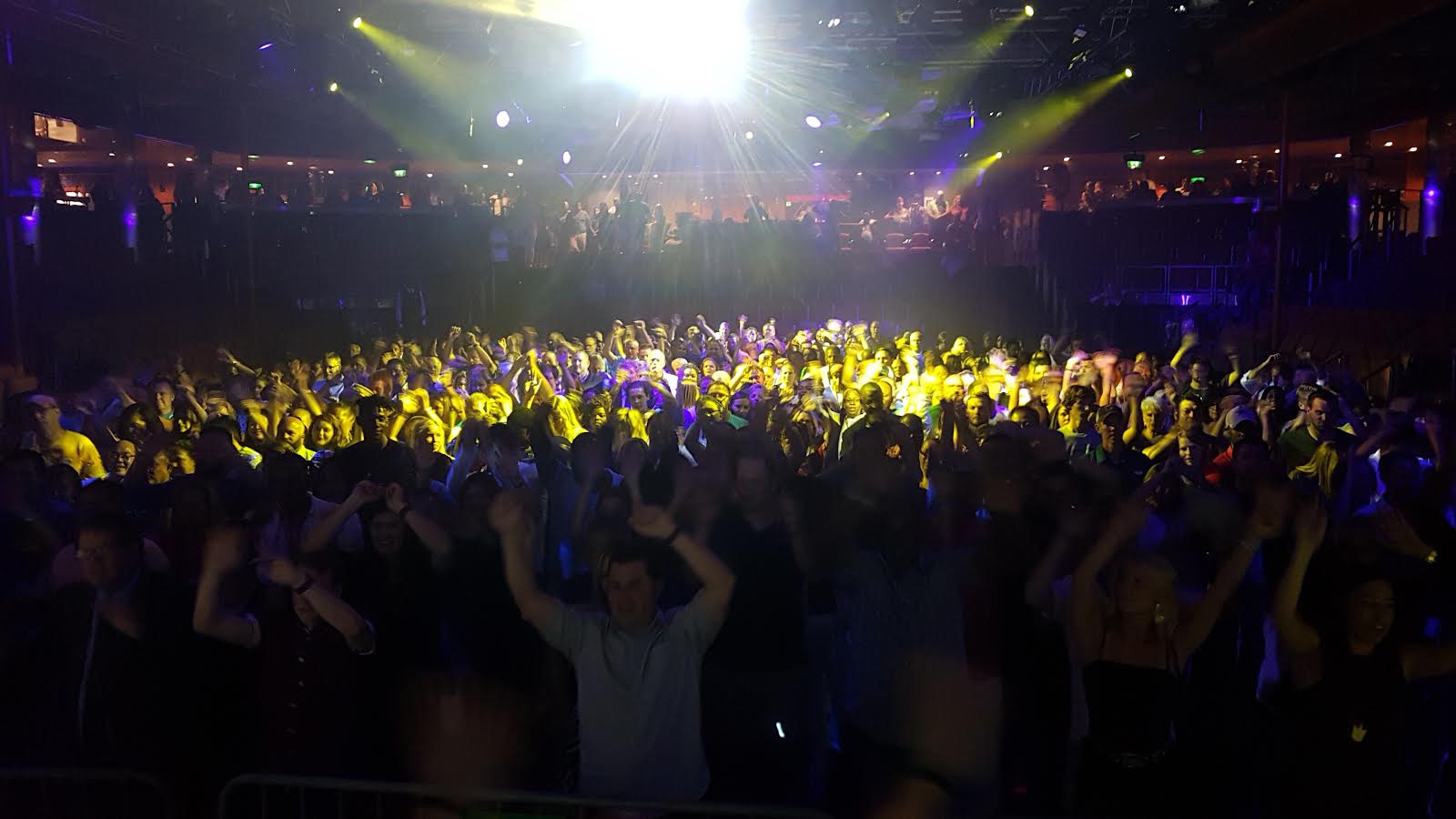 Packed dancefloor with crowd hands in the air under stage lighting